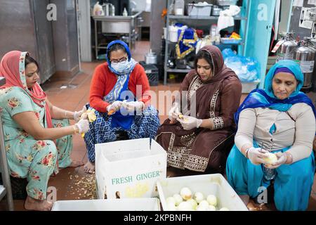 Sikh-Frauen schneiden Ingwer und Zwiebeln, die in einer Langar serviert werden, eine Gemeinschaftsküche in einem Queens Tempel, die kostenloses Essen für alle bietet. Stockfoto