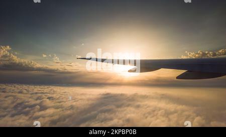 Vom Flugzeug aus blickte man auf die Wolken und den Sonnenuntergang. Flugzeugflügel über verstreuten Wolken Stockfoto