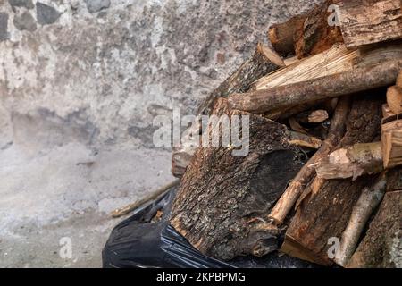 Ein Haufen Brennholz auf der rechten Seite mit grauem Hintergrund, der unscharf ist. Vorrat an alten nassbraunen Holzscheiten für Kamine und Öfen. Holz für das Heim schneiden Stockfoto