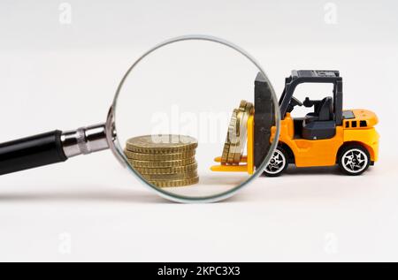 Business- und Economy-Konzept. Ein Spielzeuglader transportiert Münzen. Sehen Sie durch eine Lupe. Isoliert auf weißem Hintergrund. Stockfoto