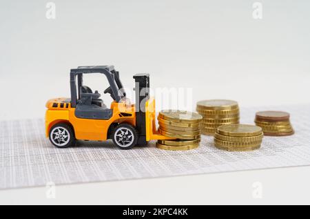 Business- und Economy-Konzept. Ein Spielzeuggabelstapler transportiert Münzen, während er durch die Buchhaltungsunterlagen fährt. Stockfoto