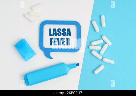 Medizin und Gesundheitskonzept. Auf einem weißen und blauen Tisch sind Pillen, ein Marker und eine blaue Plakette mit der Inschrift - Lassa-Fieber Stockfoto