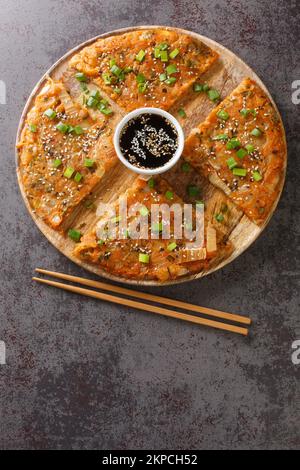 Der südkoreanische Kimchijeon-Pfannkuchen besteht aus in Scheiben geschnittenem Kimchi, serviert mit einer Dip-Sauce und mit Sesamsamen und grünen Zwiebeln bestreut Stockfoto