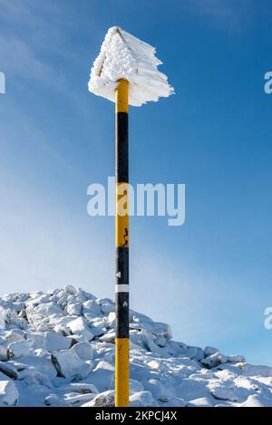 Schneebedecktes, gefrorenes Reimeis auf schneebedeckter Polmarkierung im sonnigen Winter Stockfoto