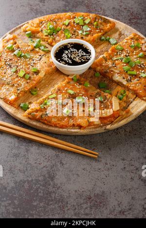 Kimchijeon im koreanischen Stil, serviert mit einer Dip-Sauce und gestreut mit Sesam und grünen Zwiebeln auf dem Holzbrett auf dem Tisch. Stockfoto