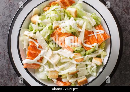 Teller mit frischem caesar-Salat mit gegrilltem Lachs, Croutons, Parmesan, Cäsar-Dressing-Nahtaufnahme auf dem Teller auf dem Tisch. Horizontale Draufsicht von abo Stockfoto
