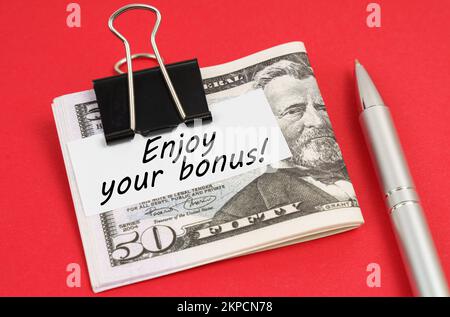 Finanz- und Geschäftskonzept. Auf rotem Hintergrund liegen ein Stift und Dollars, die mit einem Clip mit der Aufschrift auf Papier befestigt sind – viel Spaß mit Ihrem Bonus Stockfoto