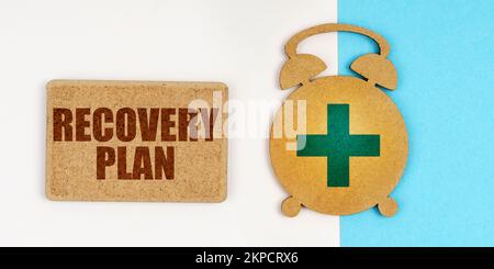 Medizin und Gesundheitskonzept. Auf der weißen und blauen Oberfläche befinden sich ein Wecker und ein Schild mit der Aufschrift - WIEDERHERSTELLUNGSPLAN Stockfoto