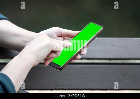 Mockup-Bild von Geschäftsleuten mit Smartphone und leerem grünen Bildschirm in einem modernen Café-Restaurant. Stockfoto