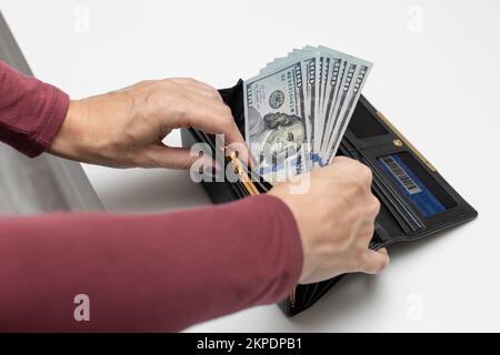 Der Mann nimmt Dollars aus seiner Brieftasche. Eine Frau, die Geld aus der Brieftasche nimmt Stockfoto