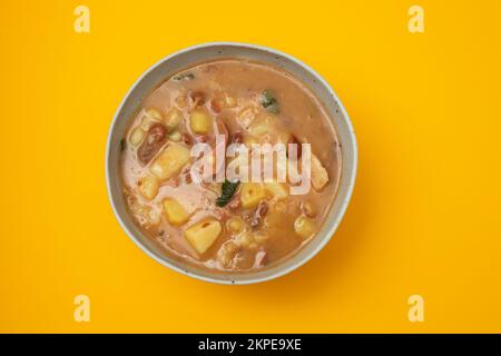 Portugiesische Steinsuppe SOPA de pedra mit Bohnen und Würstchen auf dem Teller auf gelbem Papier. Stockfoto