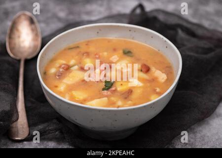 Portugiesische Steinsuppe SOPA de pedra mit Bohnen und Würstchen auf dem Teller auf Grau. Stockfoto