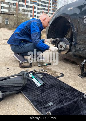 Ein Mann repariert ein Auto auf der Straße und tauscht Bremsscheiben und -Beläge aus. Maschinenausfall. Stockfoto