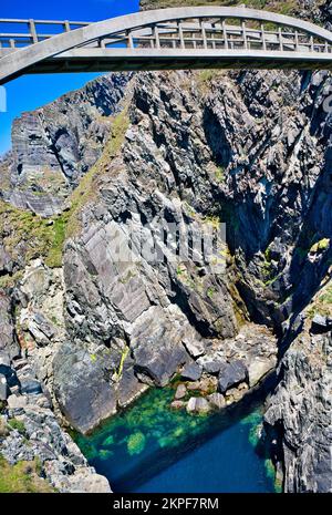 Fußgängerbrücke aus Stahlbeton über eine dramatische Meeresschlucht, die Cloghane Island mit dem Festland verbindet, Mizen Head Peninsula, County Cork, Irland Stockfoto