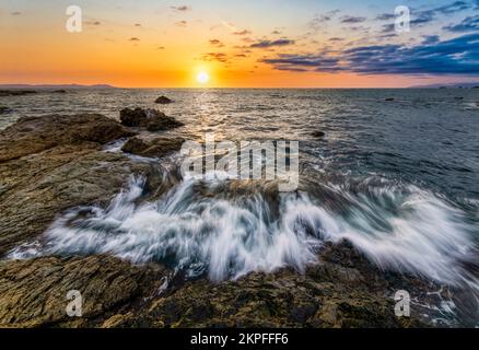 Eine Ozeanwelle bricht gegen Einen farbenfrohen Sonnenuntergang im hochauflösenden Bildformat auf Stockfoto