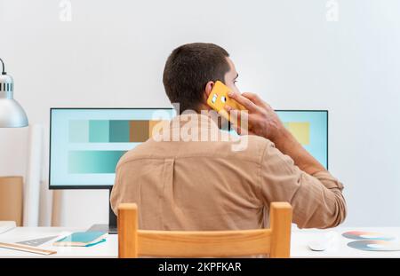 Junger Grafikdesigner, der an seinem Schreibtisch sitzt und eine Farbpalette für ein Kunstprojekt verwendet Stockfoto