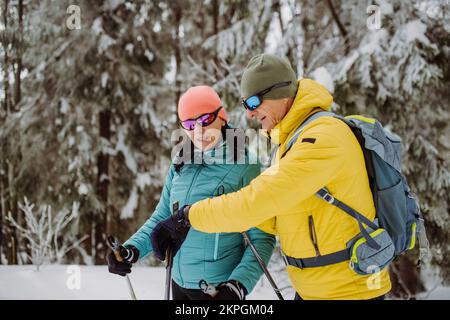 Seniorenpaar, das beim Skifahren auf Smartwatch schaut. Stockfoto