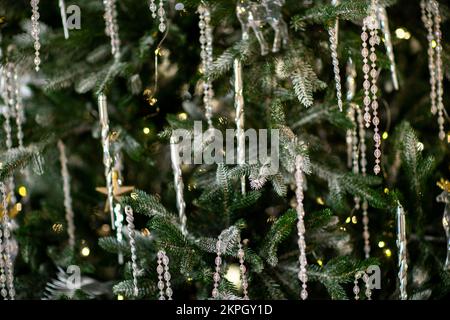 Nahaufnahme eines festlich dekorierten Weihnachtsbaums im Freien mit Bällen auf einem verschwommenen funkelnden Feenhintergrund. Unschärfe-Girlande-Lichter, Bokeh-Effekt. Stockfoto