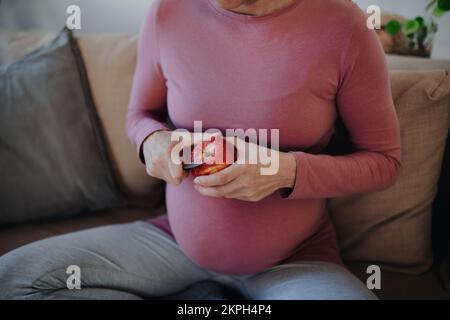 Nahaufnahme einer schwangeren Frau, die Apfel schneidet. Stockfoto