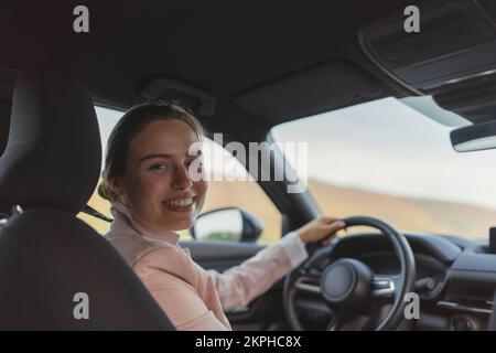 Rückansicht einer jungen Frau, die ihr Elektroauto fährt. Stockfoto