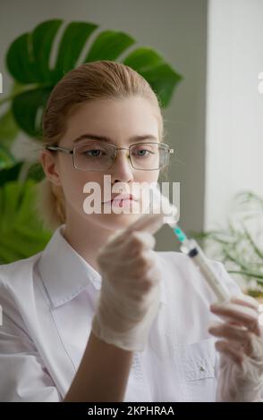 Frau in medizinischer Uniform mit einer Injektionsspritze in der Hand. Arzt oder Krankenschwester bei der Arbeit. Wissenschaftler und naturwissenschaftliche Konzepte. Nahaufnahme, selektiver Fokus Stockfoto