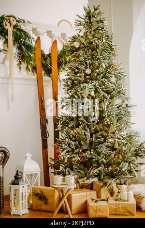 Neujahr 2022, weihnachten. Haus Zimmer für die Feiertage eingerichtet. Ein großer Baum zu Hause, viele Geschenke unter dem Baum und Skier Stockfoto