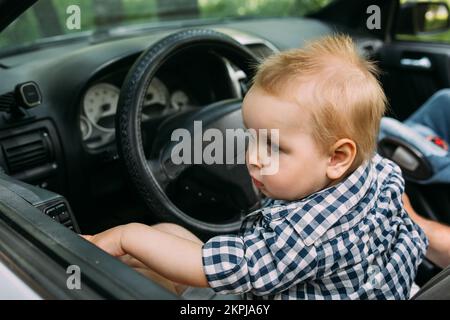 Papa zeigt seinem kleinen Sohn, wie er das Auto fährt, während er hinter dem Steuer sitzt Stockfoto