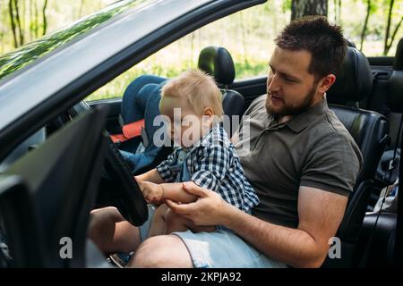 Papa zeigt seinem kleinen Sohn, wie er das Auto fährt, während er hinter dem Steuer sitzt Stockfoto