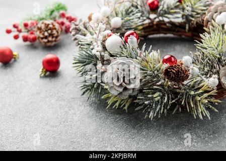 Dekorativer festlicher Weihnachtskranz. Kranz aus Tannenbaum und Zapfen auf grauem Betonhintergrund. Weihnachtsdekorationen Stockfoto