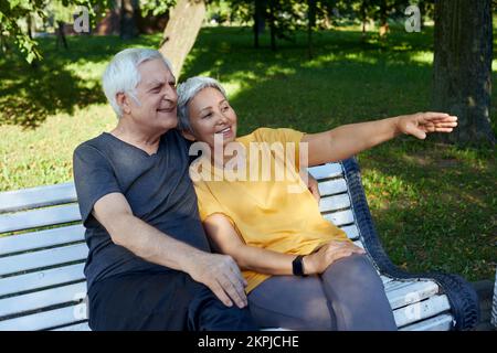 Ziemlich multirassische ältere Menschen 60s Paar sitzen auf der Bank im Park nach einem Spaziergang, Morgenspaziergang lächelnd genießen Gespräch entspannen im Freien diskutieren jemand. Passend f Stockfoto