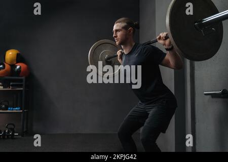 CrossFit-Athlet, der die Hantelglocke in einem dunklen Fitnesscenter hebt. Funktions- und Schaltkreistrainingkonzept. Speicherplatz kopieren Stockfoto