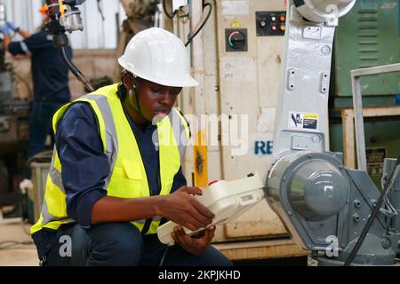 Robotikingenieur, der an der Wartung des modernen Roboterarms im Fabriklager arbeitet Stockfoto
