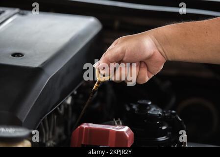 Man zieht den Ölmessstab mit der Hand nach oben, um den Motorölstand im Motor zu prüfen, Wartungskonzept für Fahrzeuge. Stockfoto