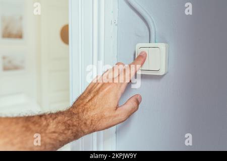 Männliche Hand drückt alten Retro-Lichtschalter im Wohnzimmer, selektiver Fokus Stockfoto