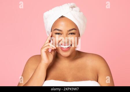 Wunderschöne afroamerikanische Übergröße mit weißem Handtuch auf dem Kopf, genießt ihre junge Schönheit und lächelt vor der Kamera Stockfoto