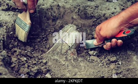 Archäologische Ausgrabungen, Archäologen arbeiten, graben ein altes Tonartefakt mit speziellen Werkzeugen im Boden Stockfoto