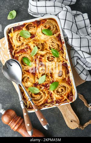 Lasagne. Hausgemachte Lasagne Pasta Rotolo mit Tomatensauce, Frischkäse und Basilikum auf weißer Pfanne auf dunklem Schiefer, Stein oder Beton. Es Stockfoto