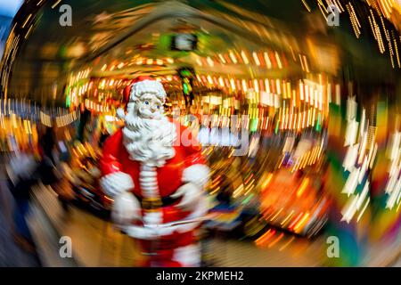 28. November 2022, Hessen, Frankfurt/Main: Eine lebensgroße Figur des Weihnachtsmanns steht auf einem Kinderkarussell auf dem Frankfurter Weihnachtsmarkt (aufgenommen mit zirkulär bewegter Kamera und längerer Belichtungszeit). Foto: Frank Rumpenhorst/dpa Stockfoto