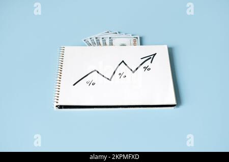 Steigende Lebenshaltungskosten, Inflation, Finanz- und Wirtschaftskrisenkonzept. Öffne das Notizbuch mit Geldscheinen und einem Pfeil, der blau aufgeht Stockfoto