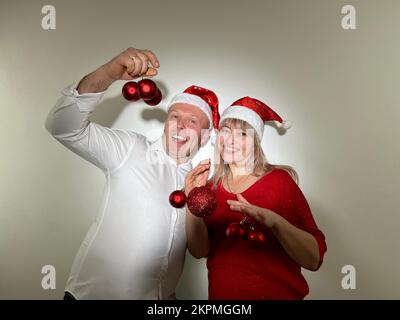 Partyeinladung Neujahr und Weihnachtsmann und -Frau Erwachsene tanzen in den Händen mit Spielzeug, haben Weihnachtshüte auf dem Kopf und rote Bälle Ded Moroz Weihnachtsmann Schneemädchen Stockfoto