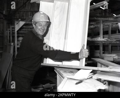 1980er, historisch, ein Baumeister mit Schutzhelm in einem Gebäudelager mit einer kleinen Holztreppe, die in ein neues Haus in England, Großbritannien, eingebaut werden soll. Stockfoto