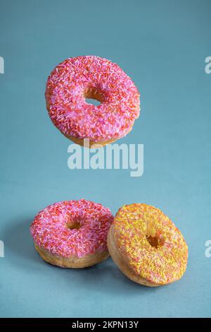 Pinkfarbene und gelbe Donuts, isoliert auf blauem Hintergrund. Stockfoto