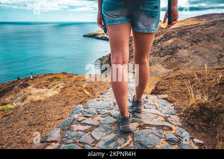 Beschreibung: Beine einer sportlichen Frau, die auf einem gepflasterten Wanderweg mit malerischer Aussicht in den wunderschönen Ausläufern der Insel Madeira spaziert. São Lourencalo, Ma Stockfoto