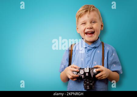 Glücklicher kleiner Junge mit Retro-Kamera auf blauem Hintergrund mit Kopierraum. Fotografiekurse Stockfoto