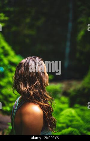 Beschreibung: Sportliche Frau bewundert einen beeindruckenden Wasserfall im Dschungel mit wunderschönen Blumen und Farnen. Levada von Caldeirão Verde, Insel Madeira Stockfoto