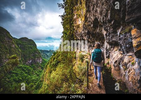 Beschreibung: Sportliche Frau mit Rucksackwanderungen auf einem abenteuerlichen Dschungelweg entlang des Kanals. Levada Caldeirão Verde, Insel Madeira, Portugal, EUR Stockfoto