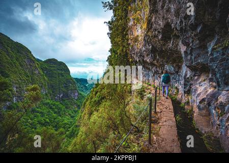 Beschreibung: Sportliche Frau mit Rucksackwanderungen auf einem abenteuerlichen Dschungelweg entlang des Kanals. Levada Caldeirão Verde, Insel Madeira, Portugal, EUR Stockfoto