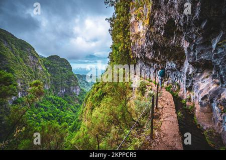 Beschreibung: Sportliche Frau mit Rucksackwanderungen auf einem abenteuerlichen Dschungelweg entlang des Kanals. Levada Caldeirão Verde, Insel Madeira, Portugal, EUR Stockfoto