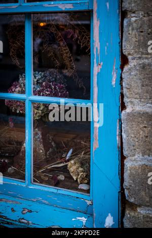 Getrocknete Blumen hinter einem verwitterten blauen Fensterrahmen. Farbenfroh und gefühlvoll. Stockfoto