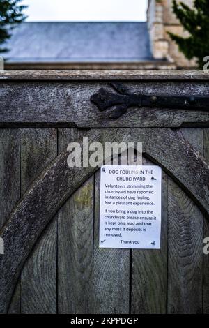 Ein Schild, auf dem die Hunde aufgefordert werden, sich nicht im Friedhof vor dem Eingang zur Powerstock Church, Dorset, England, zu verprügeln. Stockfoto